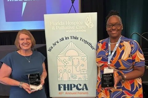 Two women holding awards next to a sign for the Florida Hospice & Palliative Care Association Annual Forum