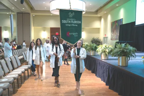 University of South Florida College of Nursing students in white coats process at a formal academic event indoors
