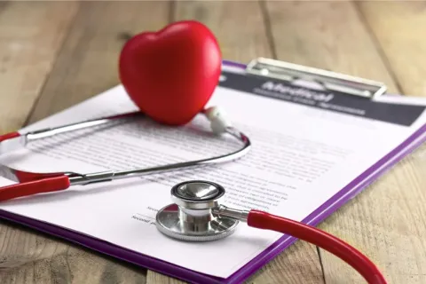 Red stethoscope and heart model on medical documents on a wooden desk representing healthcare.