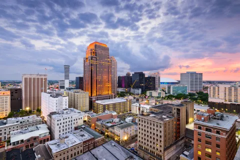 City skyline at dusk with illuminated tall buildings and a dramatic cloudy sunset sky.