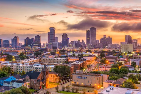 New Orleans cityscape at sunset featuring downtown skyscrapers and historic buildings under colorful skies