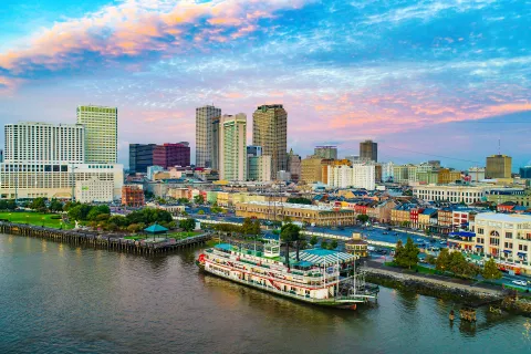 A riverboat docked by a city waterfront with skyscrapers under a colorful sunset sky.