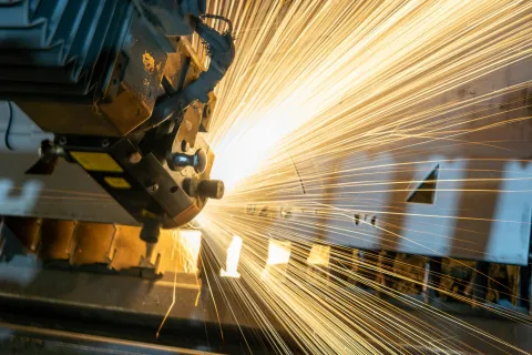 Close-up of industrial machine cutting metal with bright sparks flying in a manufacturing setting
