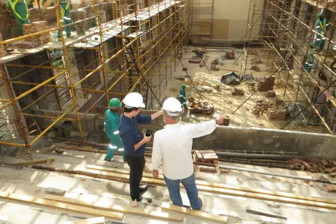 Construction supervisors wearing helmets inspecting a building site with scaffolding and workers in safety gear