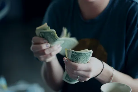 Person counting and organizing several one-dollar bills indoors with focus on hands and money.
