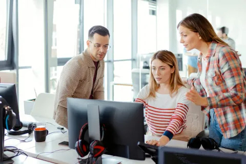 Three colleagues collaborating and discussing work while looking at a computer screen in a modern office.