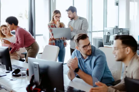 Team members collaborate and discuss projects in a bright modern office with computers and laptops
