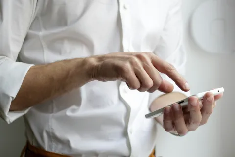 Man in white shirt using a white smartphone with one hand while tapping the screen with the other hand.