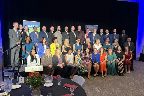Group photo of diverse professionals at a formal business event with banners in the background
