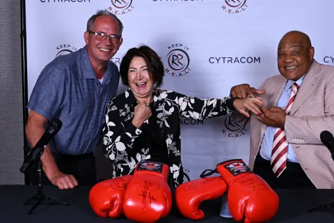 Three people smiling with signed boxing gloves, promoting Cytracom's event, Keep It R.E.A.L.