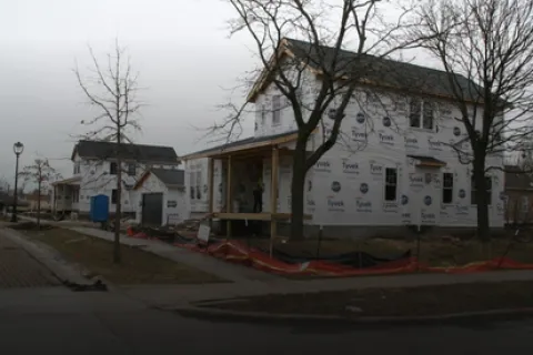 Newly constructed houses covered in Tyvek wrap on a suburban street with bare trees and overcast sky.