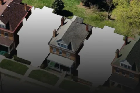 Aerial view of a residential street with brick houses and three empty plots between them.