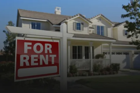 Red and white for rent sign in front of a two-story suburban house with a porch and garage on a sunny day