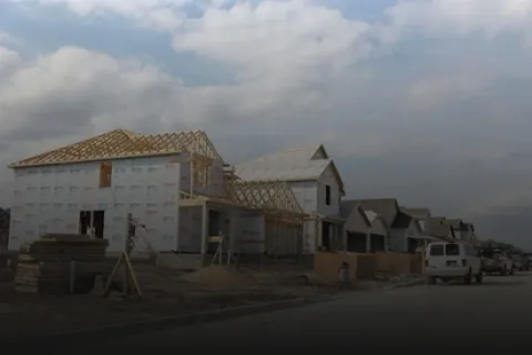 Row of houses under construction with wooden framing and building materials on a cloudy day.