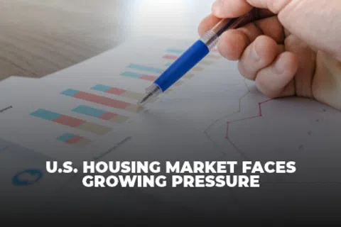 Hand holding pen over charts with U.S. housing market faces growing pressure headline