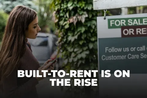 Woman looking at a real estate sign with text BUILT-TO-RENT IS ON THE RISE outdoors.