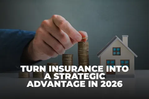 Hand stacking coins next to a model house illustrating strategic insurance growth for 2026 advantage.