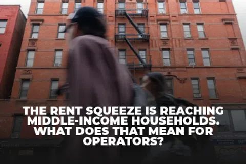 Blurred pedestrians walk past a red brick apartment building with text about rent squeeze on middle-income households.