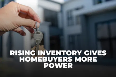 Hand holding house keys in front of a modern home with text about rising inventory empowering homebuyers.