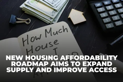 Notebook with housing affordability question, cash, small house model, and calculator on dark desk.
