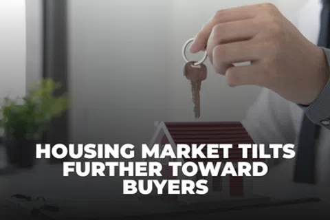 Person holding a key above a small house model with text about housing market favoring buyers.