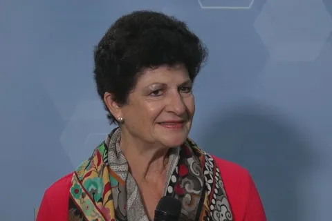 Smiling woman with short curly hair wearing a colorful scarf and red top holding a microphone