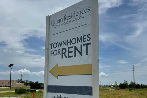 Quinn Residences townhomes for rent sign with arrow and website Live-Moccasin.com on grass roadside.