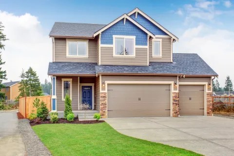 Modern two-story house with blue and beige siding, three-car garage, and landscaped front yard under blue sky.