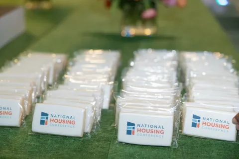 Rows of National Housing Conference branded cookies wrapped in plastic on a green tablecloth.