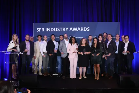 Group of award winners posing on stage at the SFR Industry Awards event with trophies and blue backdrop.