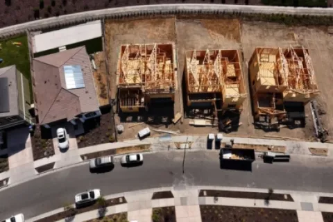 Aerial view of three wooden houses under construction next to completed homes in a residential neighborhood.