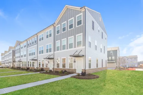 Modern three-story townhouses with gray siding and large windows on a sunny day with green lawns.