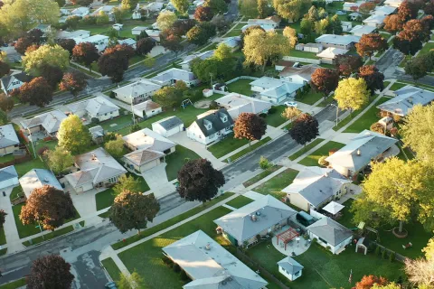 Aerial view of a suburban neighborhood with houses, streets, and trees in early autumn light.