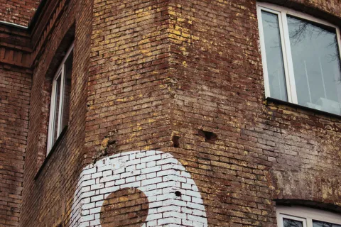 White number 9 painted on corner of aged red brick building with three windows and decorative brickwork.