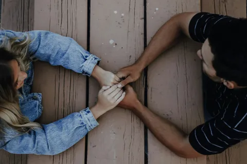 Couple holding hands across wooden table showing affection and connection, viewed from above