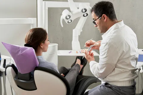 Dentist explaining dental implant model to patient seated in dental chair in modern clinic.