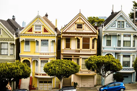 Row of colorful Victorian houses with ornamental details and trees in front on a sunny day