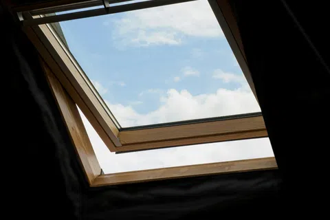 Open roof window with wooden frame showing blue sky and white clouds outside