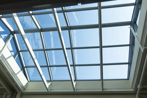 Modern ceiling skylight with large glass panels and white metal beams letting in natural daylight.