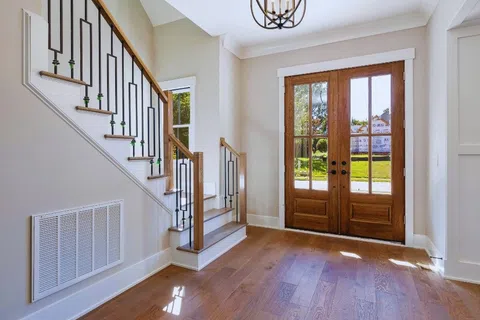 Bright modern entryway with wooden double doors, hardwood floors, and staircase with metal railings.