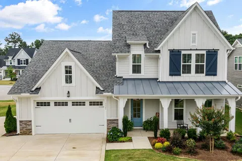 Modern two-story white house with gray roof, blue front door, garage, and landscaped front yard under a blue sky.