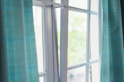 Partially open white-framed window with blue checkered curtains and soft natural light outside.