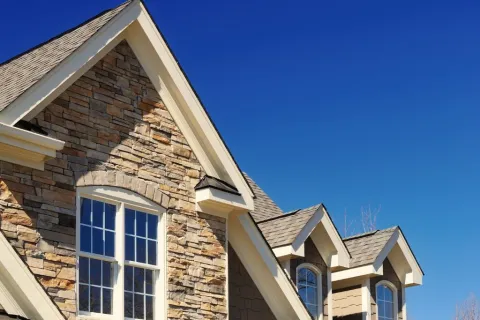 Close-up of a stone and shingle house exterior with white-trimmed windows under a clear blue sky