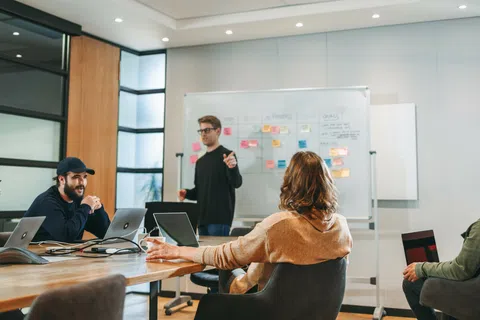 Team brainstorming session with five diverse professionals collaborating around a conference table and whiteboard with sticky notes.