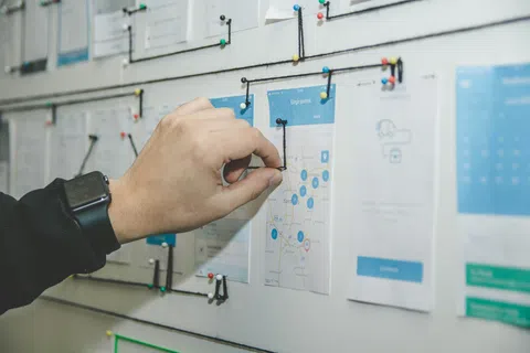 Hand placing black string on a wall map connected with pins and strings for project planning or analysis.