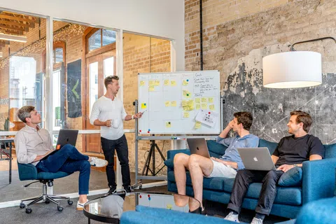 Team meeting in modern office with whiteboard planning and laptops, brainstorming ideas and collaboration