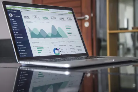 Laptop displaying data analytics dashboard with graphs, charts, and statistics on a reflective black table.