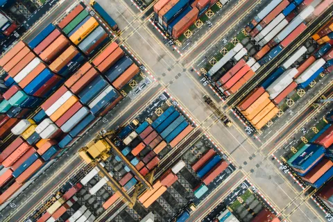 Aerial view of colorful shipping containers arranged at a busy port with cranes and marked lanes.