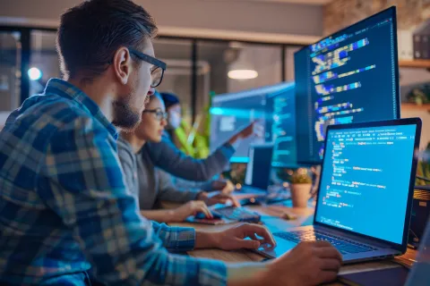 Software developers working collaboratively on coding projects with multiple monitors displaying code.