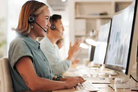 Customer service representatives wearing headsets working on computers in a bright modern office.